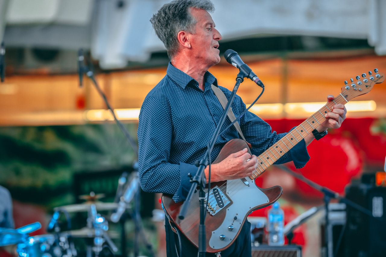 Pjevač i gitarist ADONAI-ja pjeva na mikrofon pod toplim svjetlima pozornice.